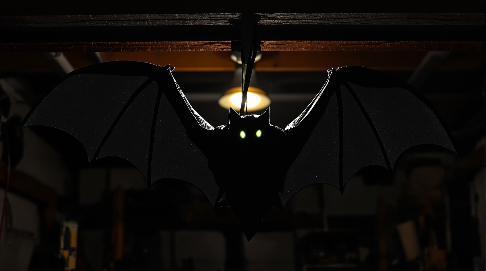 A finished homemade bat prop hanging in a dark garage with faintly glowing eyes