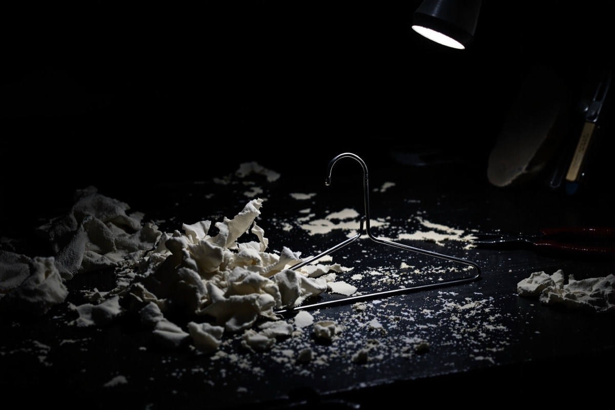 A bent coathanger ghost frame beside torn cheesecloth and pliers