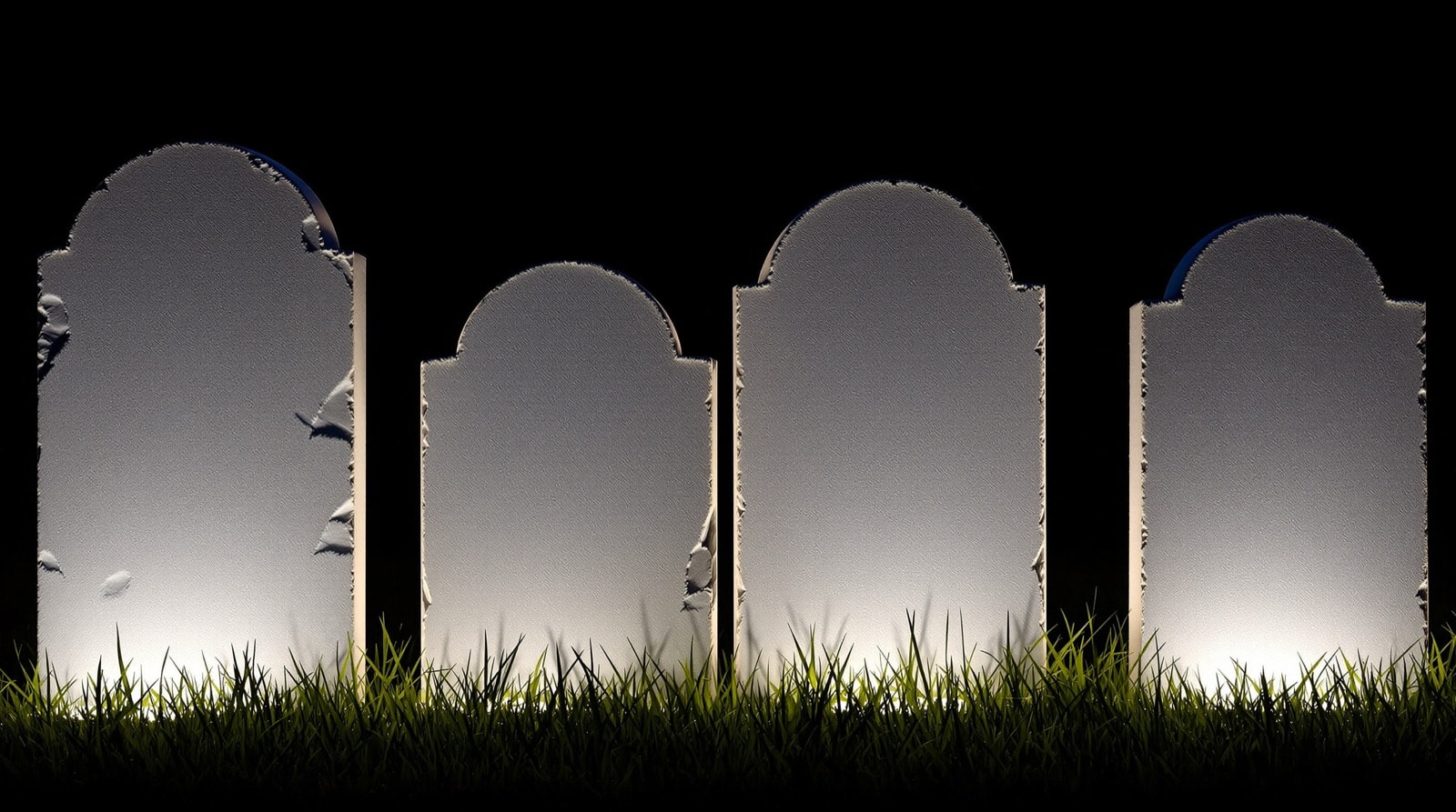 Four homemade foam tombstones in a dark lawn lit low from the side