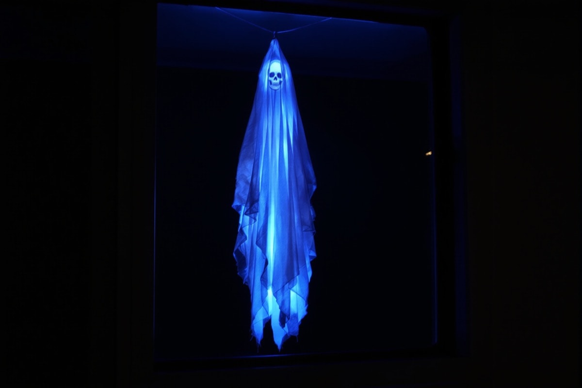 A spectre glowing under a blacklight seen through a window from outside