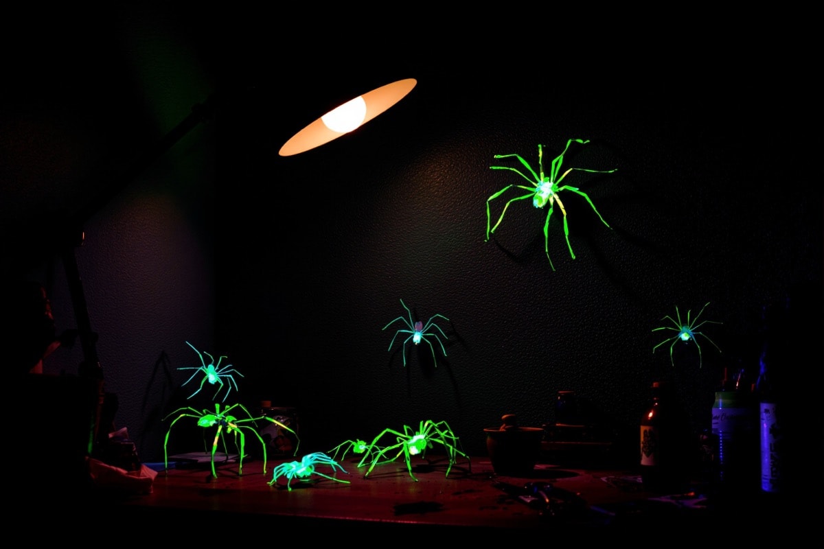 A group of homemade spiders glowing under a blacklight in a dark corner